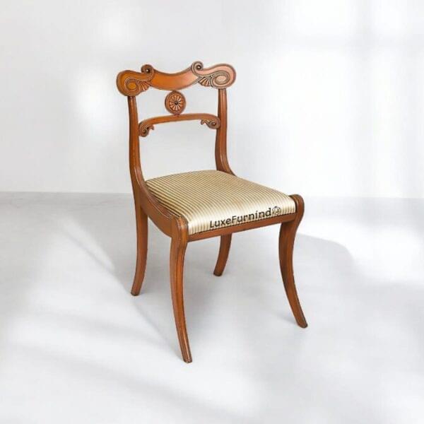 This elegant vintage Regency-style chair features curved legs and detailed backrest carving, crafted with fine hardwood and striped fabric – a refined piece of handcrafted furniture from Indonesia.